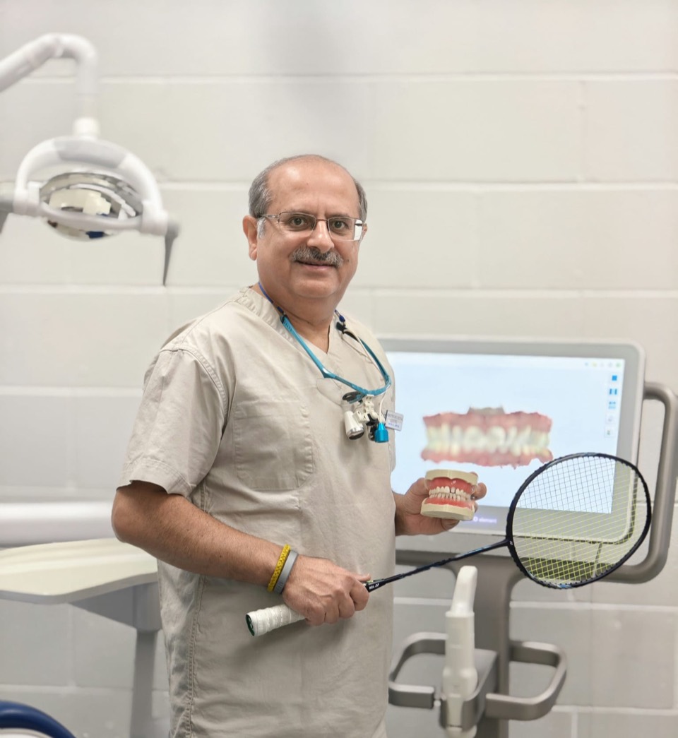 Dr. Rakesh Arya in his dental office, holding a badminton racket and a dental model